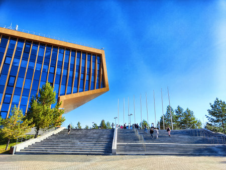 Visitors gather around modern architecture and flagpoles in the bustling Innopolis Innovation City under clear skies.の写真素材