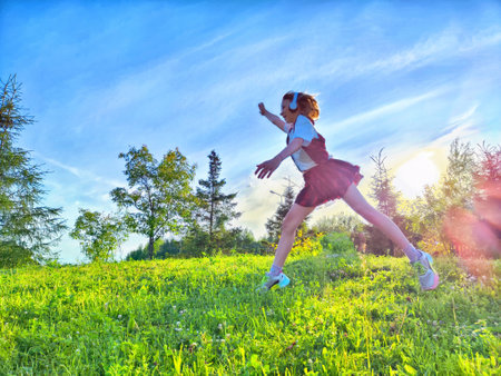 Young girl joyfully running through a green meadow during sunset with bright blue skies