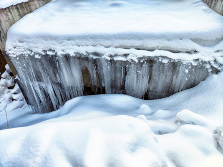 Snow blankets a concrete surface while icicles hang down, creating a serene winter scene in a cold environment.の写真素材
