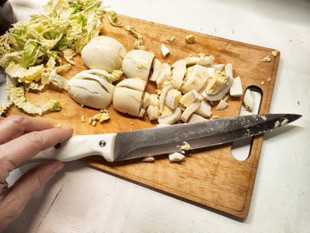 Hand chopping boiled eggs and cabbage on a wooden cutting board ready for cooking a nutritious dish.の写真素材