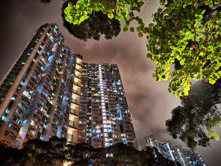 Tall residential buildings illuminate the night in Hong Kong, with vibrant lights contrasting...