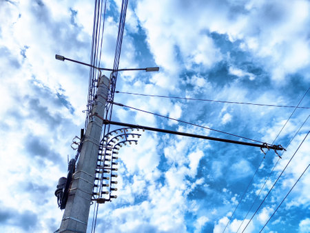 A tall electric pole supports numerous wires against a backdrop of dynamic clouds, capturing the...