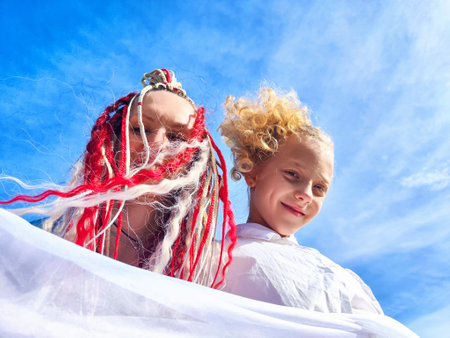 Two cheerful individuals with colorful hairstyles enjoying a bright day under a clear sky while holding a light fabricの写真素材