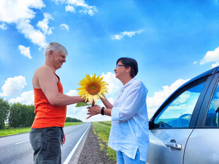 Middle-aged couple sharing a joyful moment with a sunflower during their road trip in the countrysideの写真素材