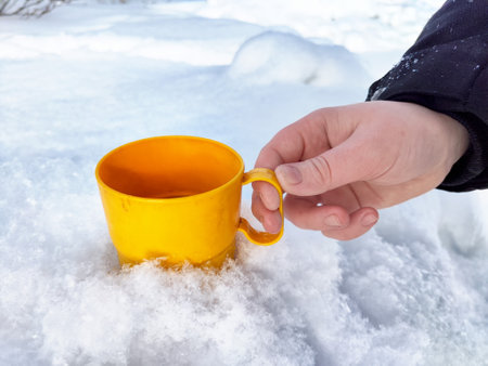 A hand grips a vibrant yellow cup nestled in soft white snow, capturing a moment of winter enjoyment outdoors.の写真素材