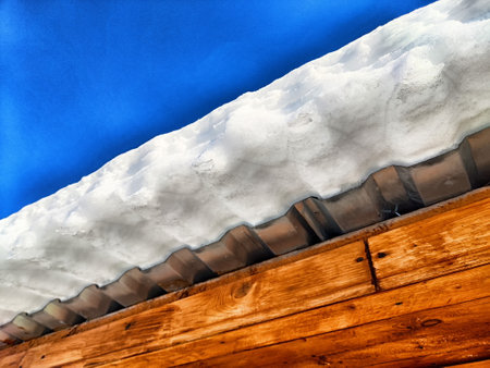 Heavy snow is perched dangerously on the edge of a roof, threatening potential ice falls as the temperature begins to rise.の写真素材