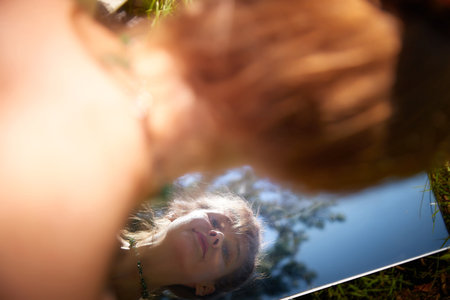 A woman in a beautiful dress, laying on the forest floor, reflected in a mirror. Environmental friendliness and caring for natureの写真素材