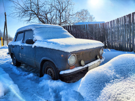 A vintage car is buried under a thick layer of snow on a frosty day, highlighting the contrast with the bright blue sky.の写真素材