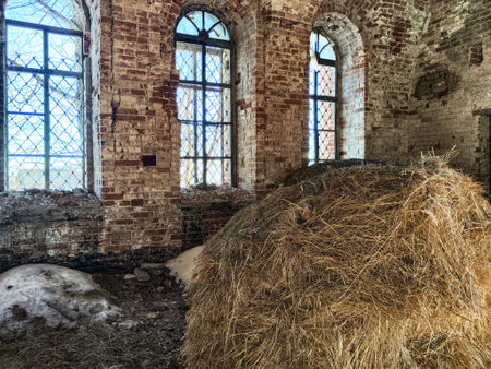 A large hay bale sits in an abandoned structure surrounded by cracked brick walls and broken windows, partially covered in snow.の写真素材