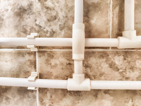PVC pipes are neatly installed on a tiled wall, showing intricate connections and a clean layout in a home setting.の写真素材
