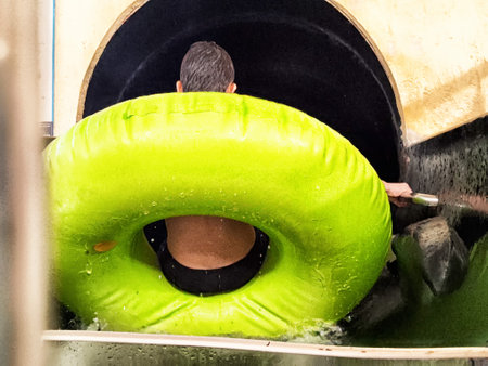 A person is poised to slide down a water chute, seated on a large green float, ready for a thrilling descent into the water.の写真素材