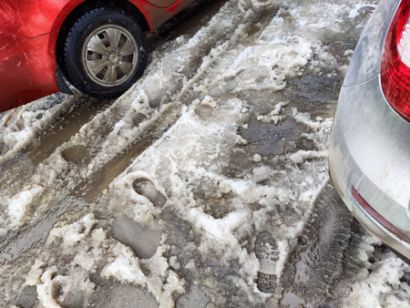 The road is partially covered in melting snow and mud, showing the transition of springtime with parked cars on the side.の写真素材