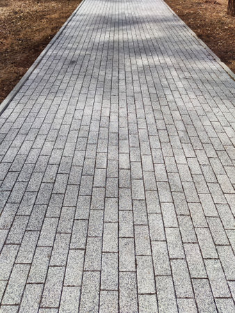 A straight, well-maintained paved walkway stretches through a serene outdoor area, surrounded by...