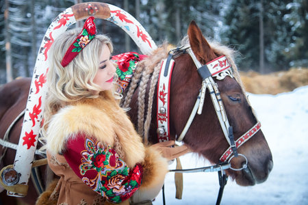 Beautiful girl in traditional dress enjoys Maslenitsa holiday with her horse in winter setting