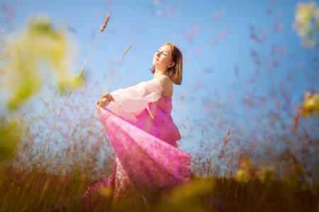 Woman in colorful dress enjoying a sunny day in a vibrant flower field surrounded by natureの写真素材
