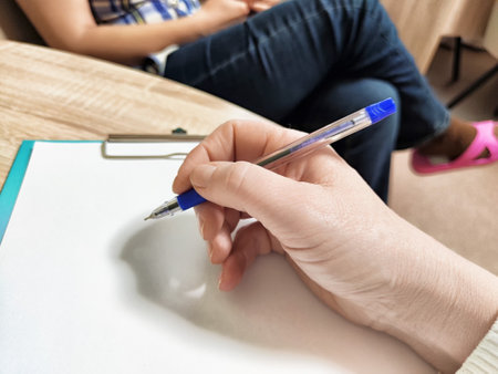 A middle-aged psychologist is poised to take notes in a therapy session, emphasizing active listening in a professional office setting.の写真素材