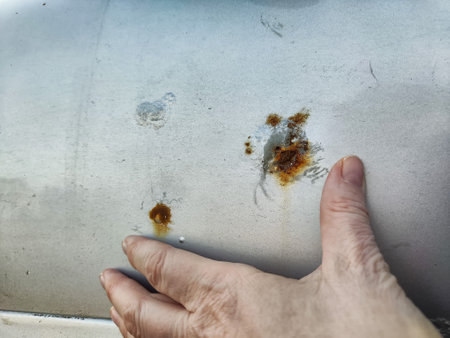 Close-up view of rust patches on a car surface. A hand gently touches the affected area,...