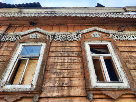 Display of an old wooden structure showcasing intricate designs on windows and faded paint under a clear sky in late afternoon.の写真素材