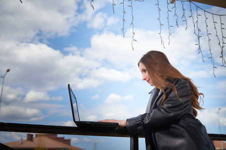 Young woman working on a laptop outdoors with a beautiful sky in the backdropの写真素材