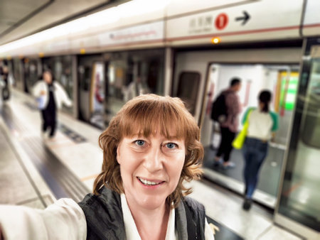 Blonde woman captures a selfie inside a subway station, surrounded by fellow travelers while enjoying her exploration of a vibrant city.の写真素材
