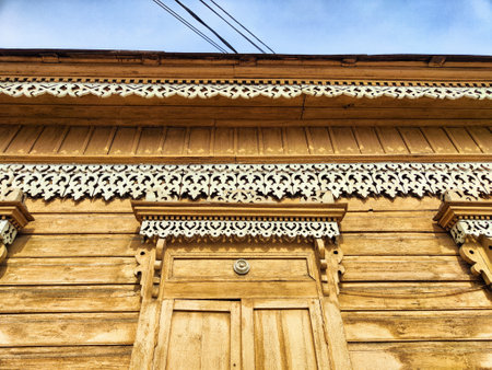 Intricate wooden carvings adorn the facade of an old house under a bright blue sky, showcasing traditional architectural artistry.の写真素材