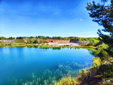 Turquoise water glistens under a clear blue sky at a tranquil quarry site, framed by lush green vegetation and serene landscapes.の写真素材