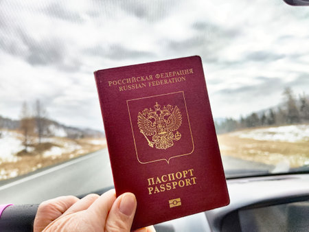 Passport of a Russian citizen is held up inside a car with a blurred road and nature in the background on an overcast day.の写真素材