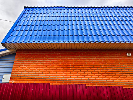 A vibrant brick wall adorned with a blue roof stands strong against a backdrop of overcast skies in a quiet neighborhood.の写真素材