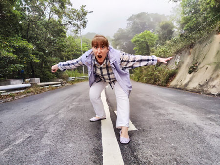 Blonde woman joyfully poses on a deserted road surrounded by fog, showing her adventurous spirit.の写真素材
