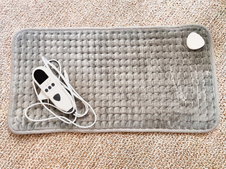 Cozy electric heating pad placed on a textured surface, ready to provide warmth and relief for tired muscles or cold days.の写真素材