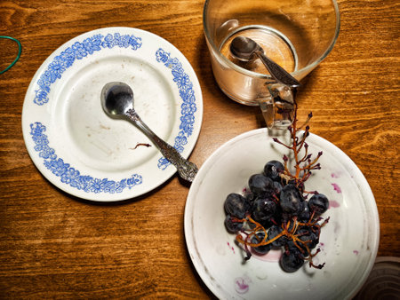 Fresh grapes are displayed on a alongside plate an empty bowl and glass, creating a relaxed dining atmosphere on a wooden table.の写真素材