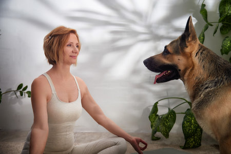 Practicing yoga indoors with a dog in a serene, green-filled space for a healthy lifestyleの写真素材