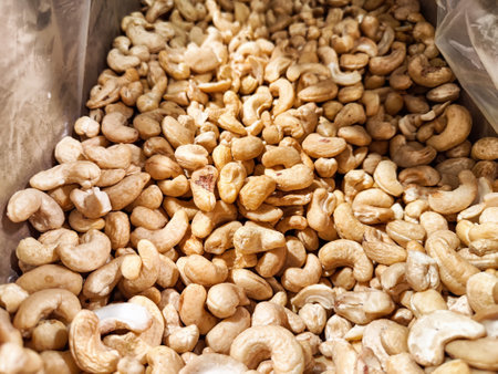 Cashew nuts are piled high in a market, showing their varied shapes and sizes under natural...
