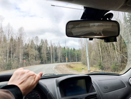A driver navigates a winding road lined with trees, showcasing lush greenery and an overcast sky in...