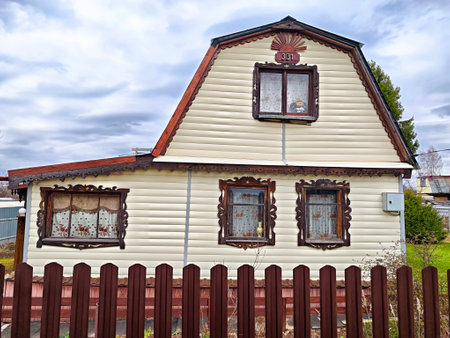 A quaint wooden house features ornate window designs and a sloping roof, set against a cloudy sky in a serene countryside location.の写真素材