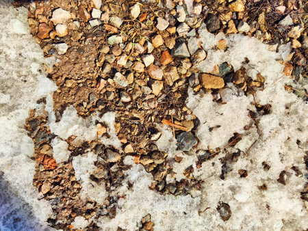 Soil and melting snow combine to form a unique texture in a natural outdoor area, showing the transition of seasons.の写真素材