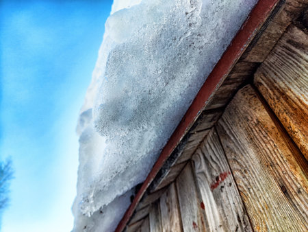 Snow accumulated on a wooden roof poses a potential danger as it melts, with icicles forming under...