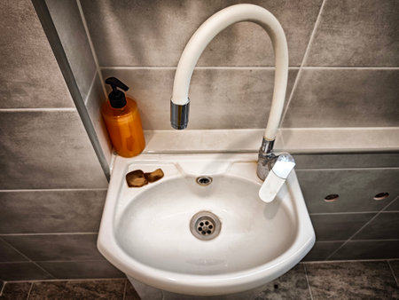 Small sink setup featuring a stylish faucet and a practical bottle on the side for easy access in a contemporary bathroom.の写真素材