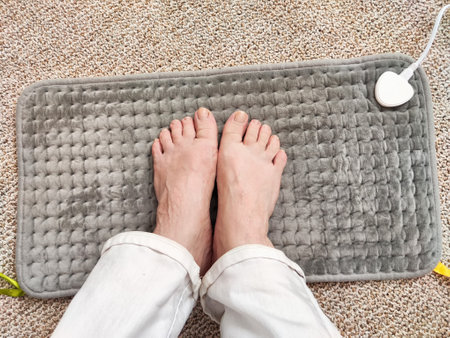 Bare feet are resting on a soft electric heating pad placed on a fluffy carpet, providing warmth and comfort in a cozy environment.の写真素材