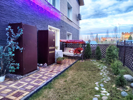 A peaceful garden area features a comfortable seating space and manicured grass, illuminated by soft lights as twilight approaches.の写真素材