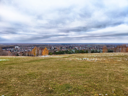 Expansive view of a town surrounded by rolling hills, showcasing vibrant autumn colors beneath a cloudy sky.の写真素材