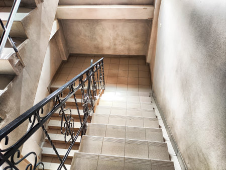 A well-lit staircase descends through a modern building, featuring clean tiles and a decorative railing, suggesting daily use by residents.の写真素材