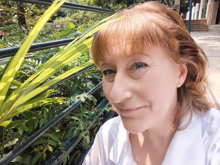 Blonde woman enjoying a sunny day at a lush location, taking a cheerful selfie while surrounded by greenery.の写真素材