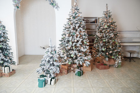 Three elegantly adorned Christmas trees are displayed in an inviting indoor space, surrounded by wrapped gifts, creating a festive atmosphere perfect for celebrations.の写真素材