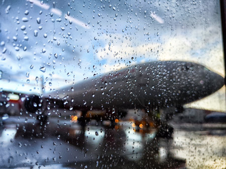 An airplane is seen on the tarmac, partially obscured by raindrops on a window during a rainy day at the airport.の写真素材