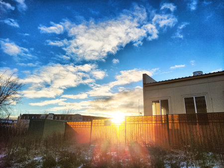Warm sunlight breaks through clouds, illuminating a serene neighborhood with a modern house as dawn approaches, showingcasing nature beauty.の写真素材