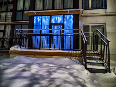 Decorative blue lights shine on an entrance surrounded by untouched snow, creating a cozy winter ambiance during the evening hours.の写真素材