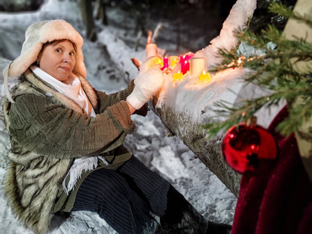 Middle-aged woman enjoying a winter night walk in the woods amidst colorful candlesの写真素材