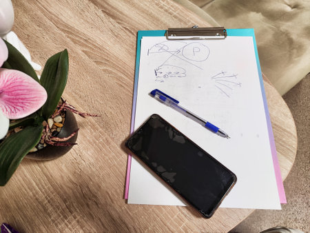 A workspace is laid out with sketch paper, a pen, a smartphone, and a small decorative plant, creating a relaxed atmosphere for creativity.の写真素材