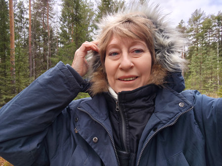 Mature woman takes a selfie in a lush forest, sharing her travel experiences and enjoying the beauty of nature during an outdoor adventure.の写真素材
